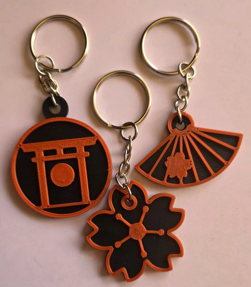 Three keychains printed in vermilion and black: a torii gate, a cherry blossom and a folding fan